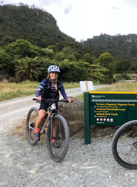 Woman standing over her bike by a roadsign smiling at the camera.