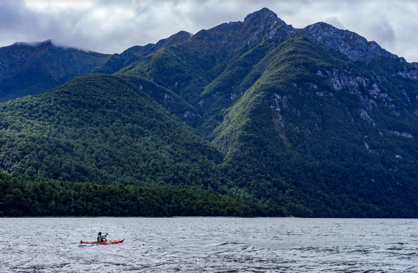 kayaking on body of water with mountains behind.