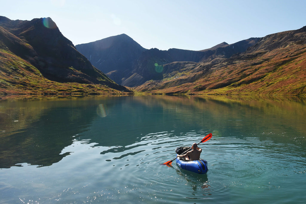 Man Packrafting on a still lake with mountains in the background