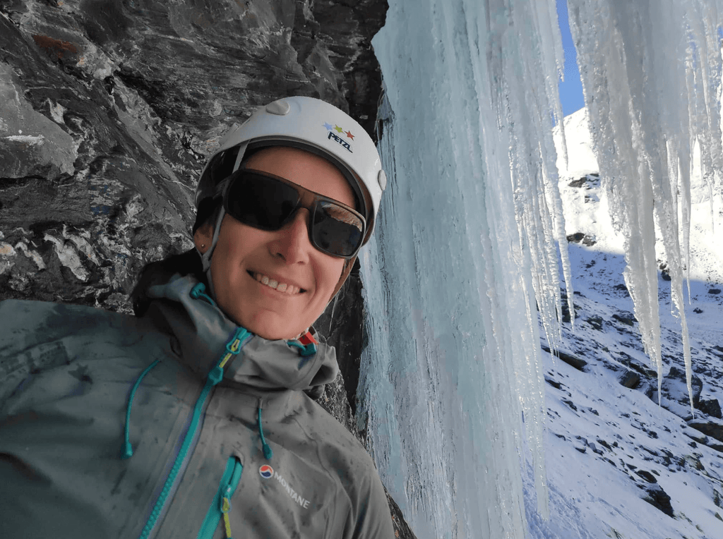 Woman in helmet staring by rock next to ice waterfall