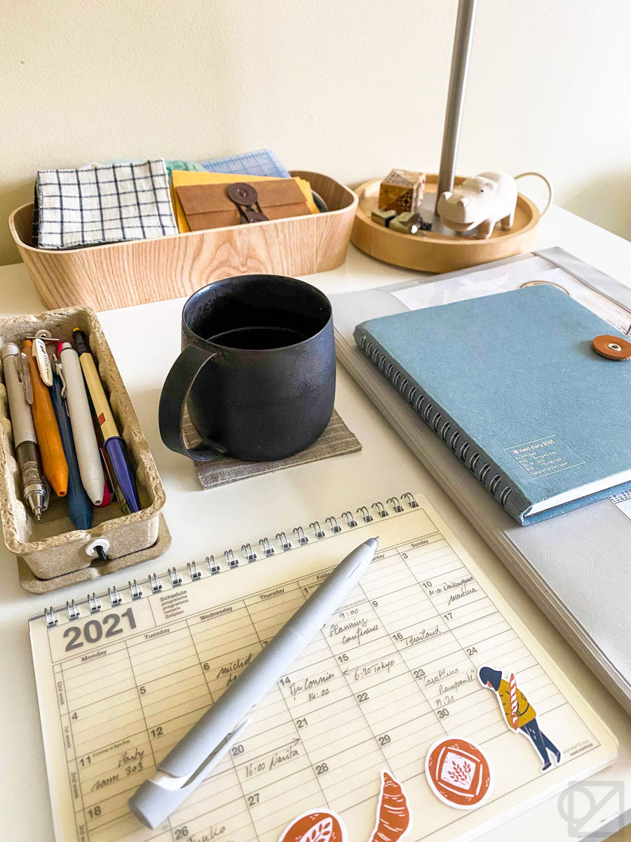 The desk with a pencil case, coffee mug, and a few books, neatly arranged in a grid.