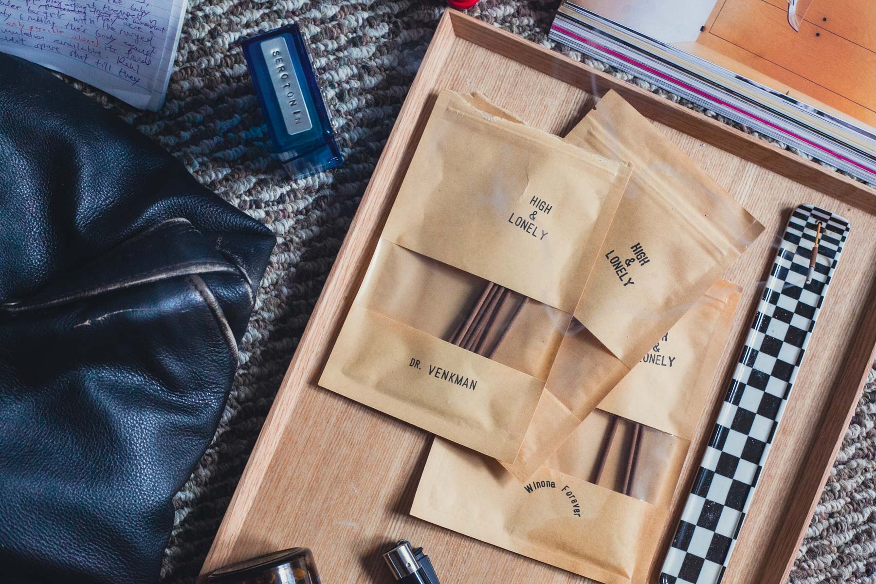 A spread of personal things on the floor, centered on 3 packs of incense on a wood tray.