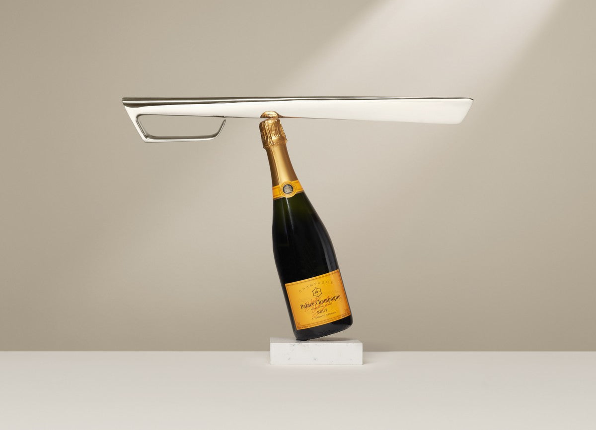 Silver champagne sabre balanced horizontally on a leaning champagne bottle.