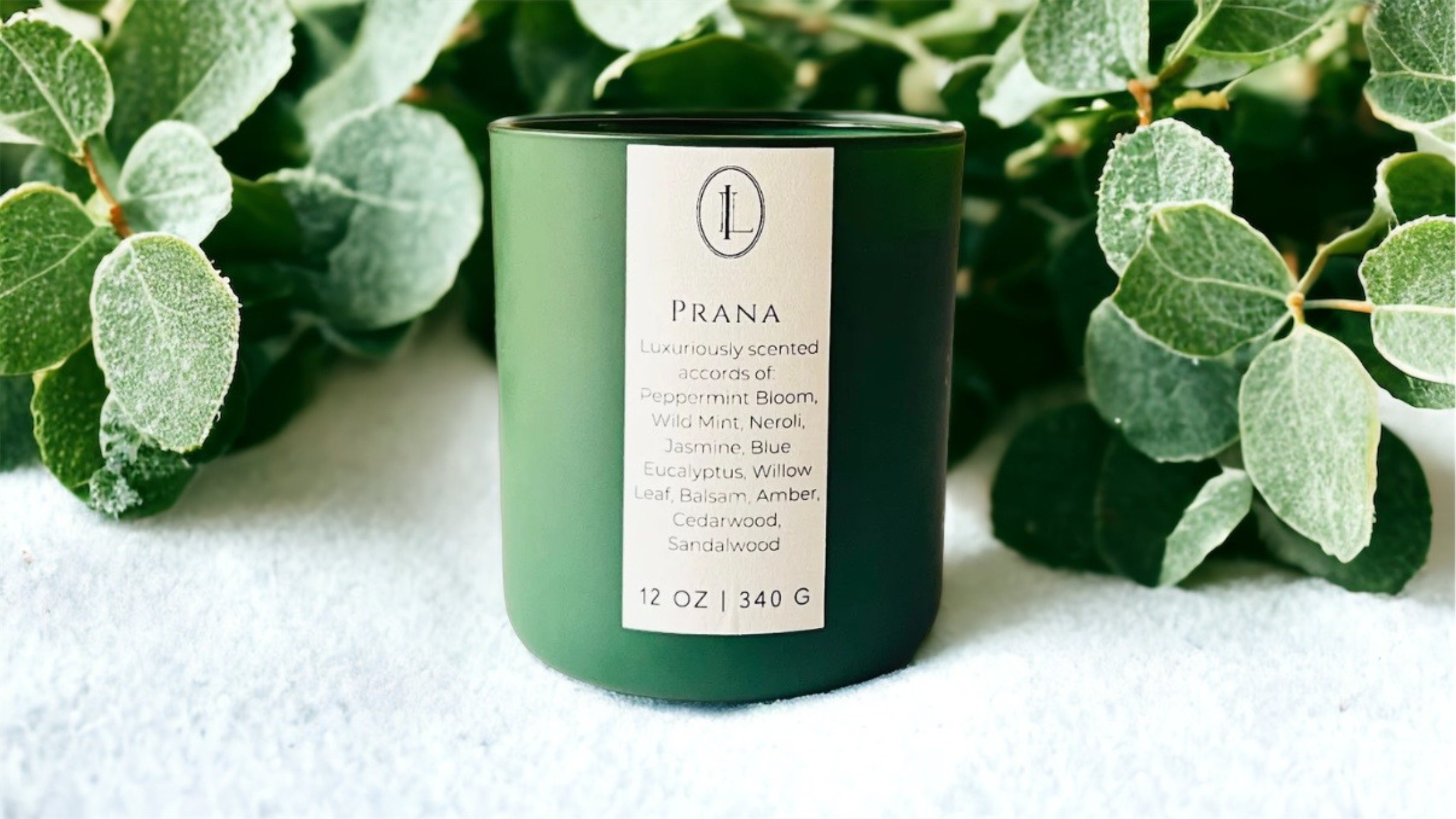 image of Prana candle sitting on snow with eucalyptus