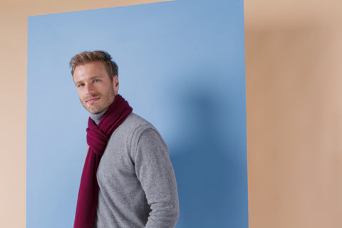 Man wearing a gray sweater and a long, red scarf, both made of pure cashmere, as he looks toward you