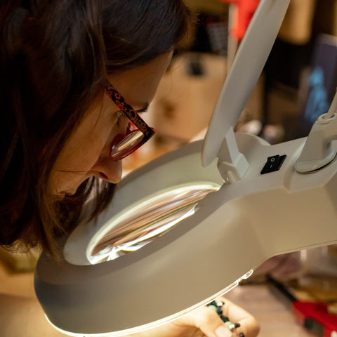Photo of Diane Kremer working on jewelry through a magnifying glass