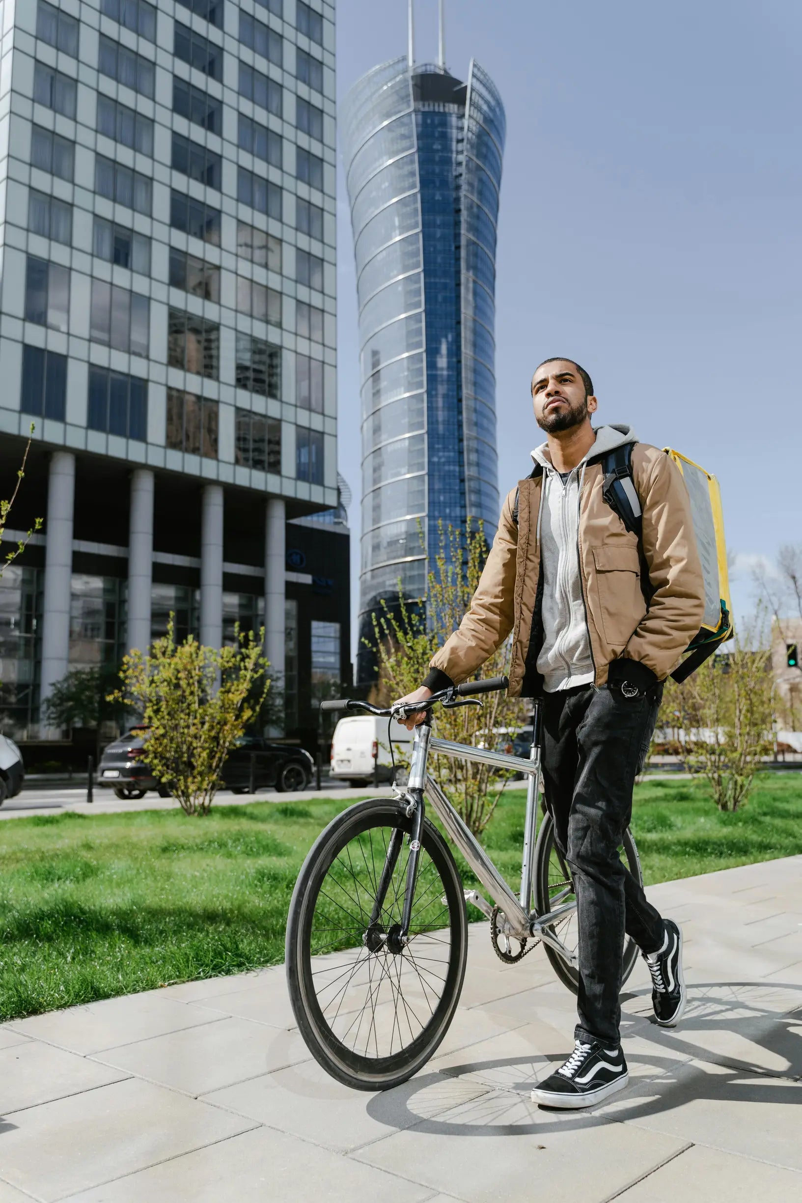A courier with a backpack walks a bicycle in modern Warsaw, delivering parcels.