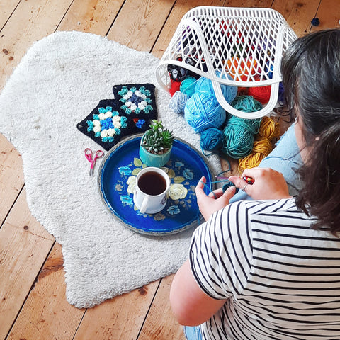 Pigeon is sat on the floor hooking crochet granny squares