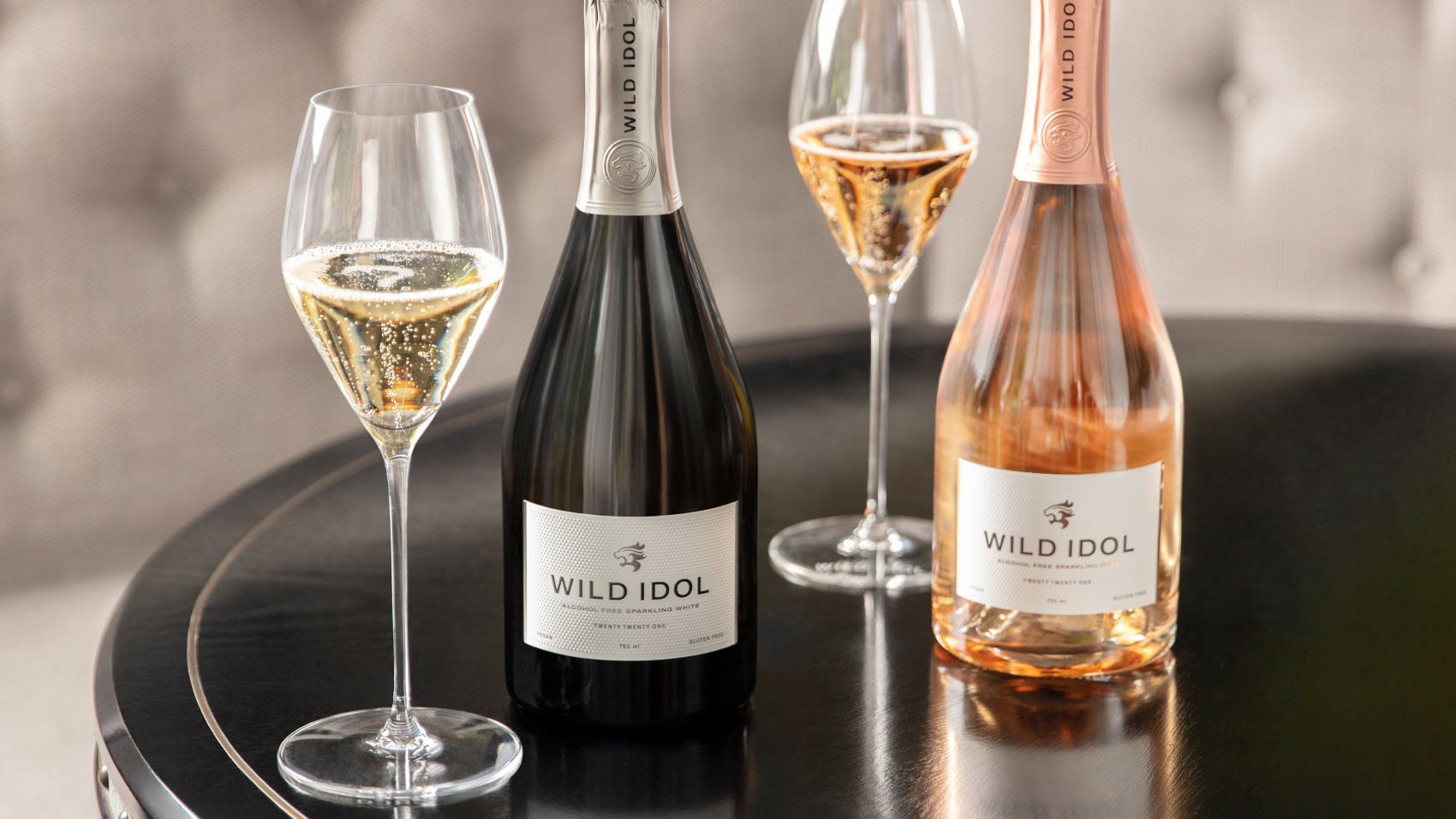 Glasses of WILD IDOL Alcohol Free Sparkling Rosé & White Wine, standing on a table, alongside their bottles