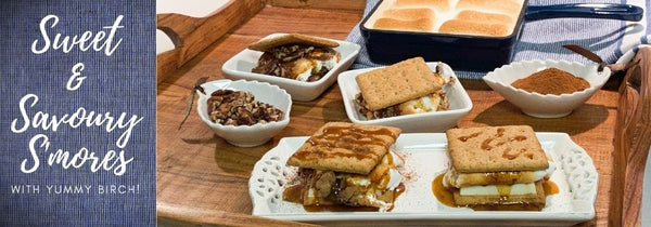 Delicious white chocolate, birch whiskey toffee sauce and cinnamon s'mores as well as chocolate, birch whiskey toffee and pecan s'mores on a nice wooden tray with toasted marshmallows in the background. The captions says "Sweet & Savory S'mores" to introduce the blog article that follows.