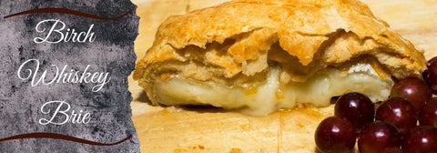 Birch Whiskey Toffee sauce and baked apples oozing out of a flakey pastry as display on a butcher block board next to lovely plump purple grapes.