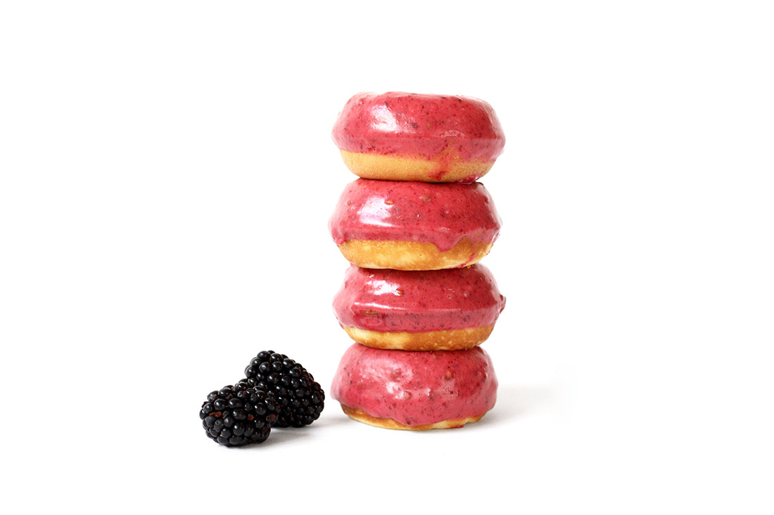 Stack of four Miss Jones Baking Co Blackberry Buttermilk Donuts next to two blackberries