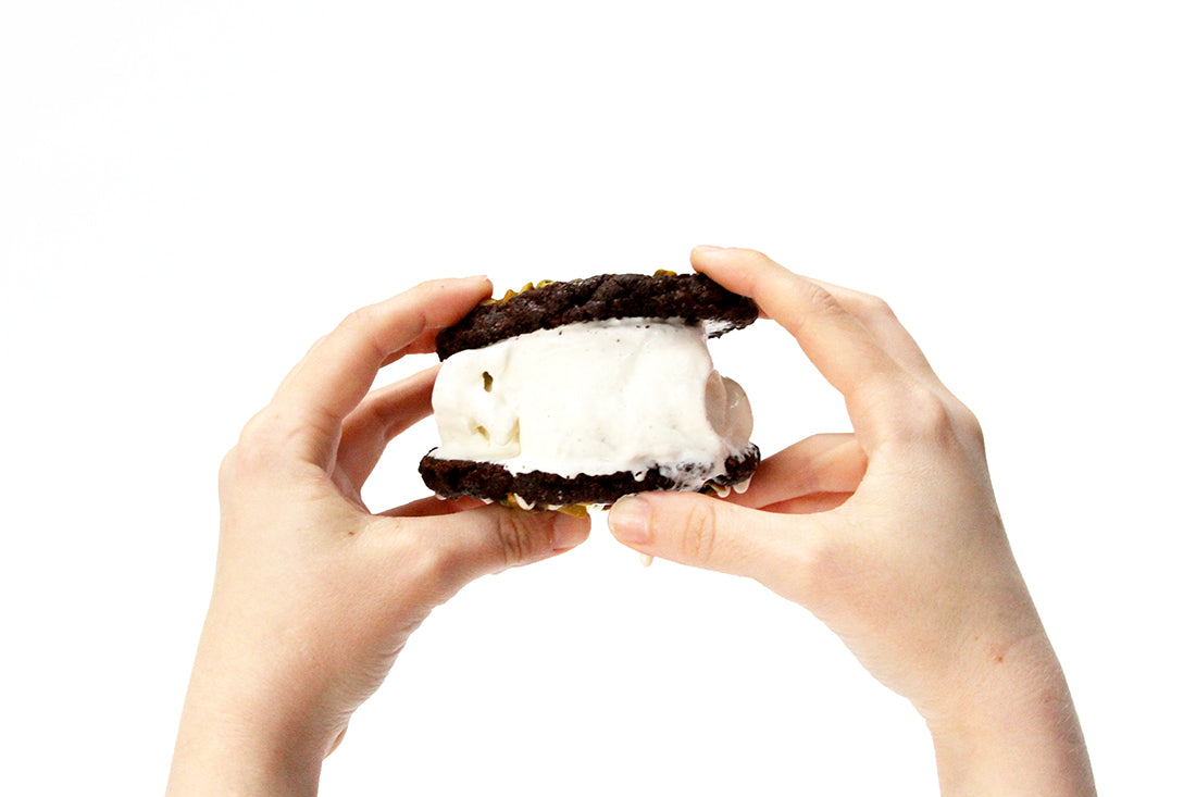 Image of two hands holding up a Miss Jones Baking Co Brownie Crisp Cookie Sandwich