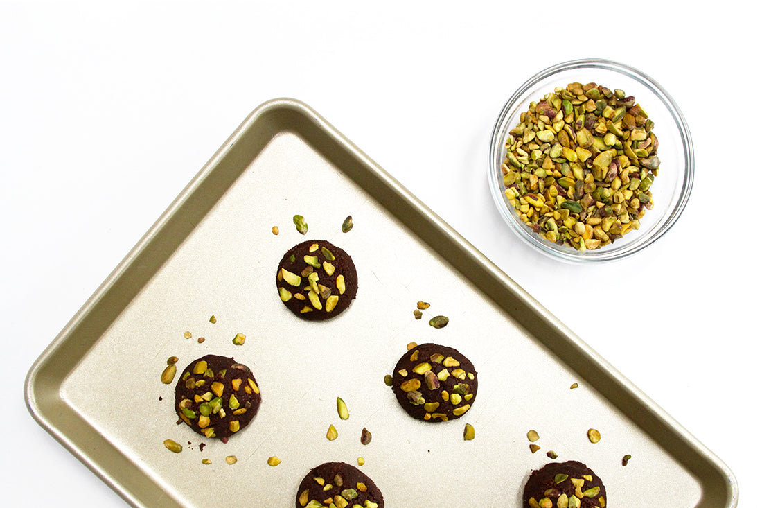 Image from above of a baking pan with five Miss Jones Baking Co Brownie Crisp Cookie Sandwiches next to a bowl of pistachios