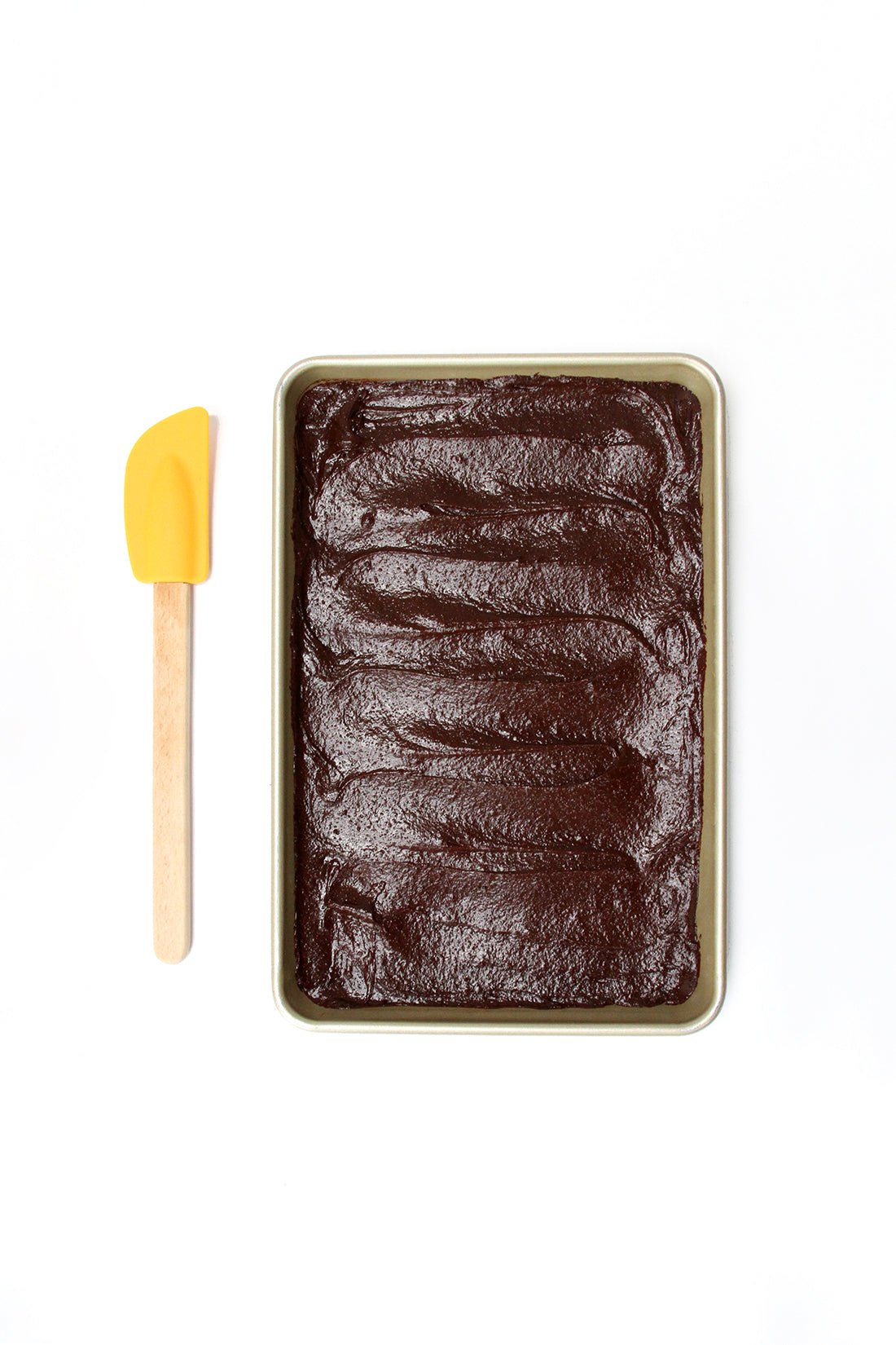 Image from above of brownie batter on a baking sheet next to a yellow spatula used for Miss Jones Baking Co Coffee Break Shake