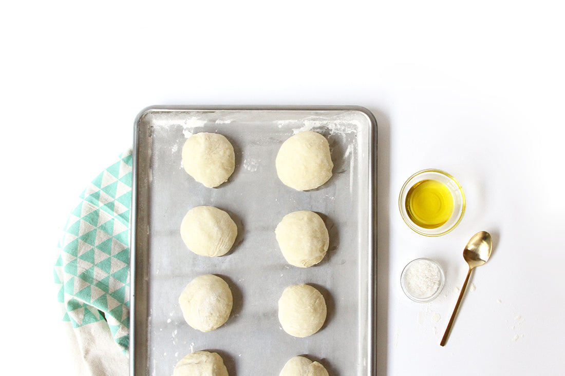 Image of baking sheet with six dough balls for Miss Jones Baking Co Cake Mix Dinner Rolls next to salt and olive oil dishes