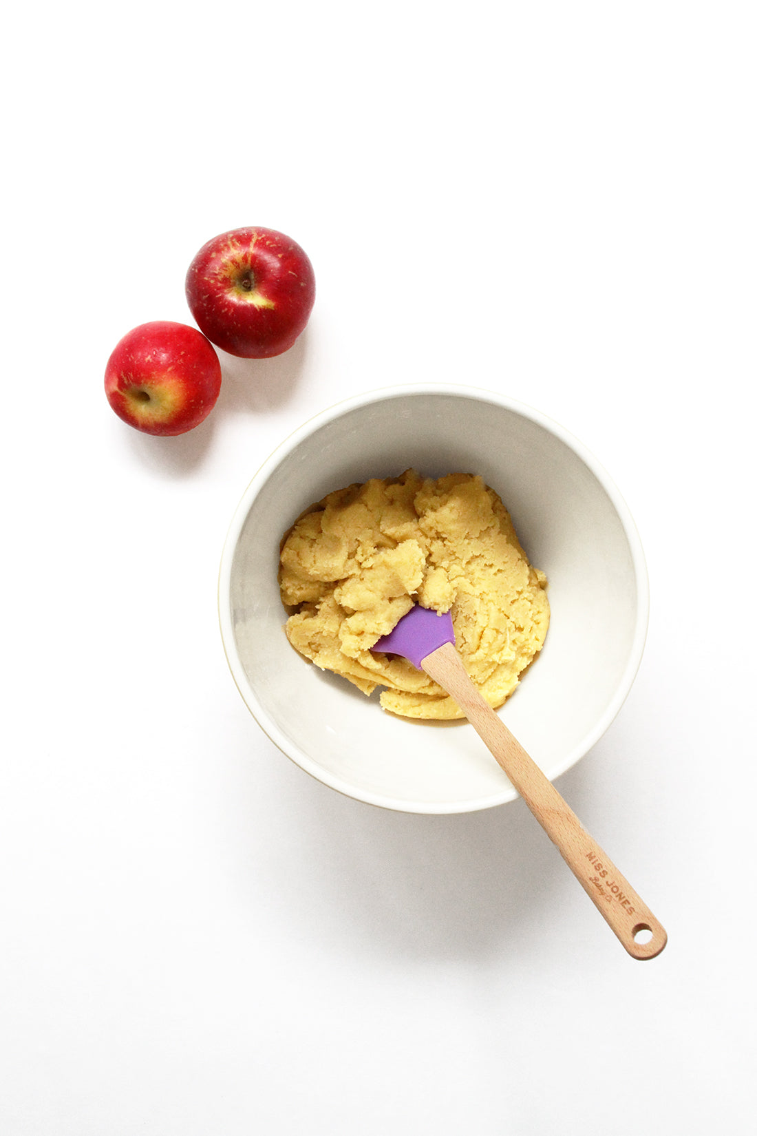 Image of a mixing bowl with batter for Miss Jones Baking Co Caramel Apple Bars next to two red apples