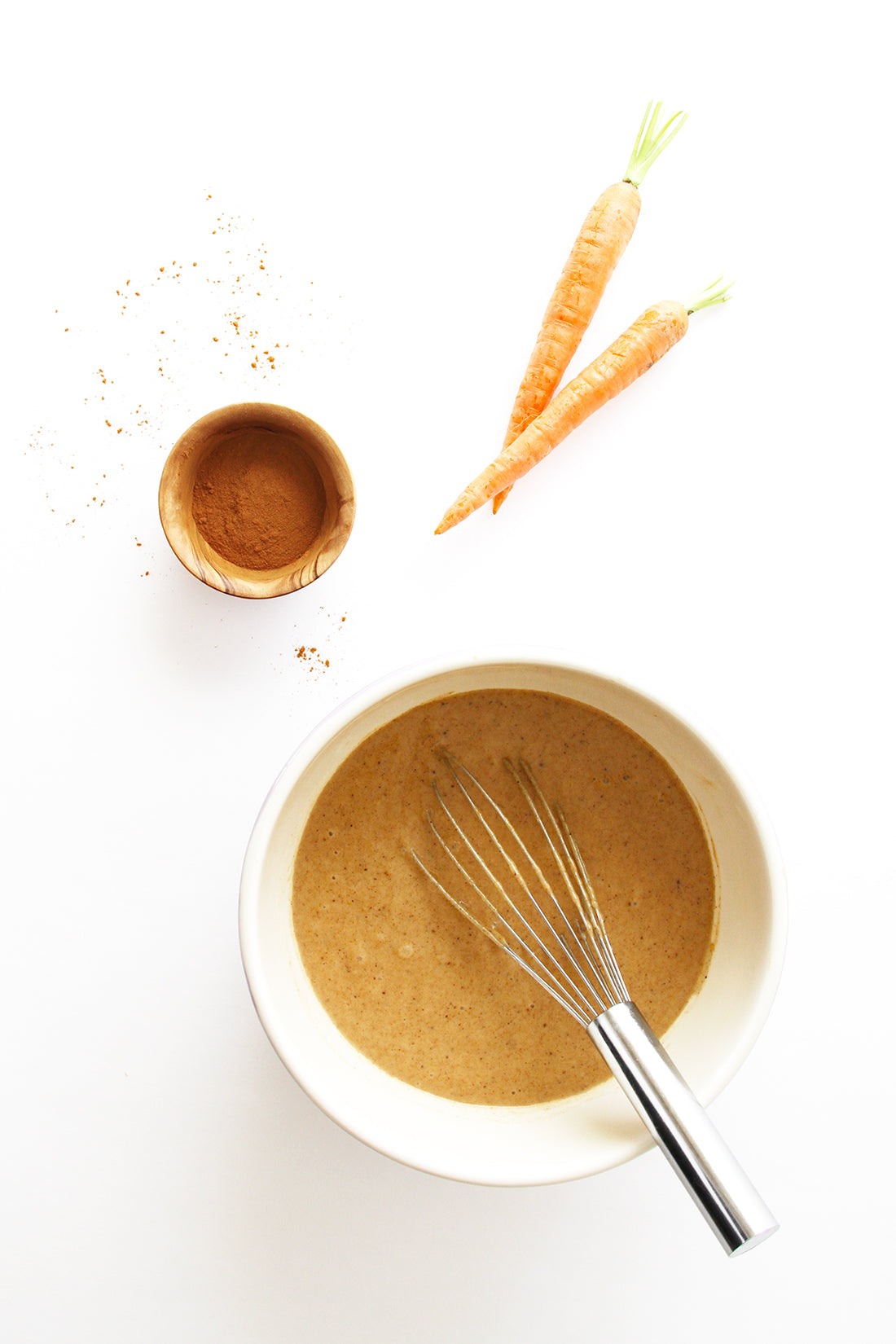 Image of a bowl of Miss Jones Baking Co Carrot Spice Cake batter next to two carrots and spice
