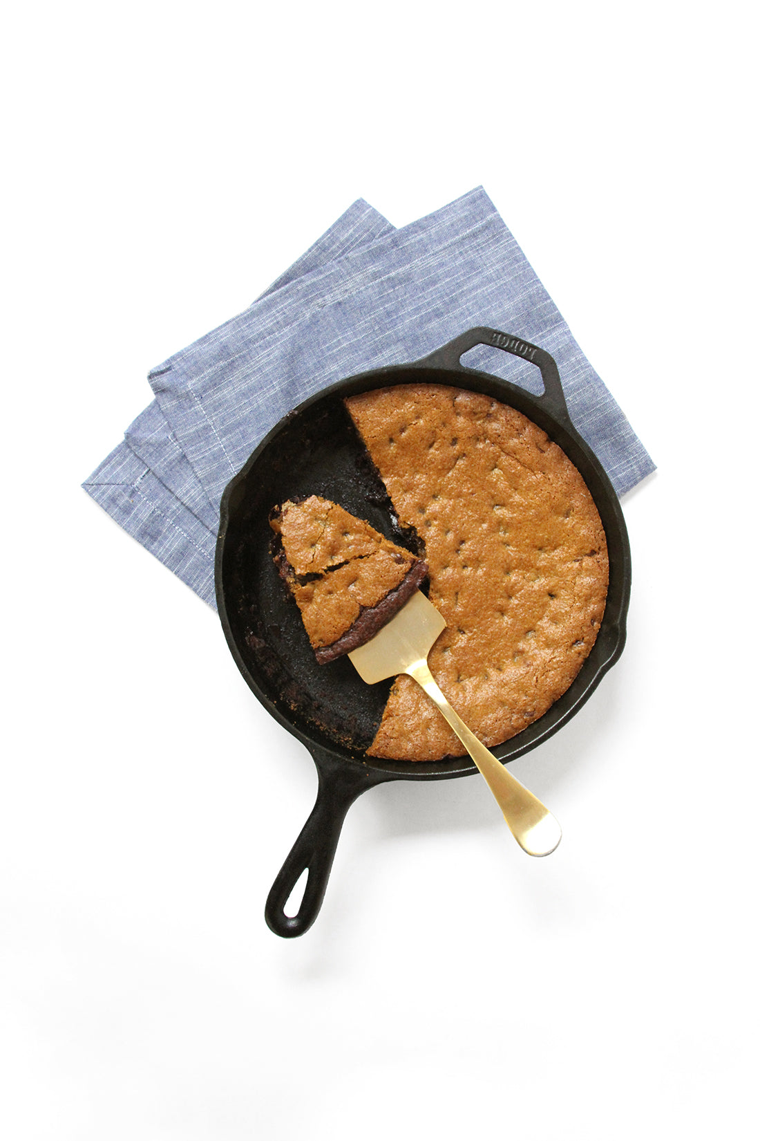 Part of Miss Jones Baking Co Chocolate Chip Brownie Skillet in the skillet with a slice on top of a golden serving utensil