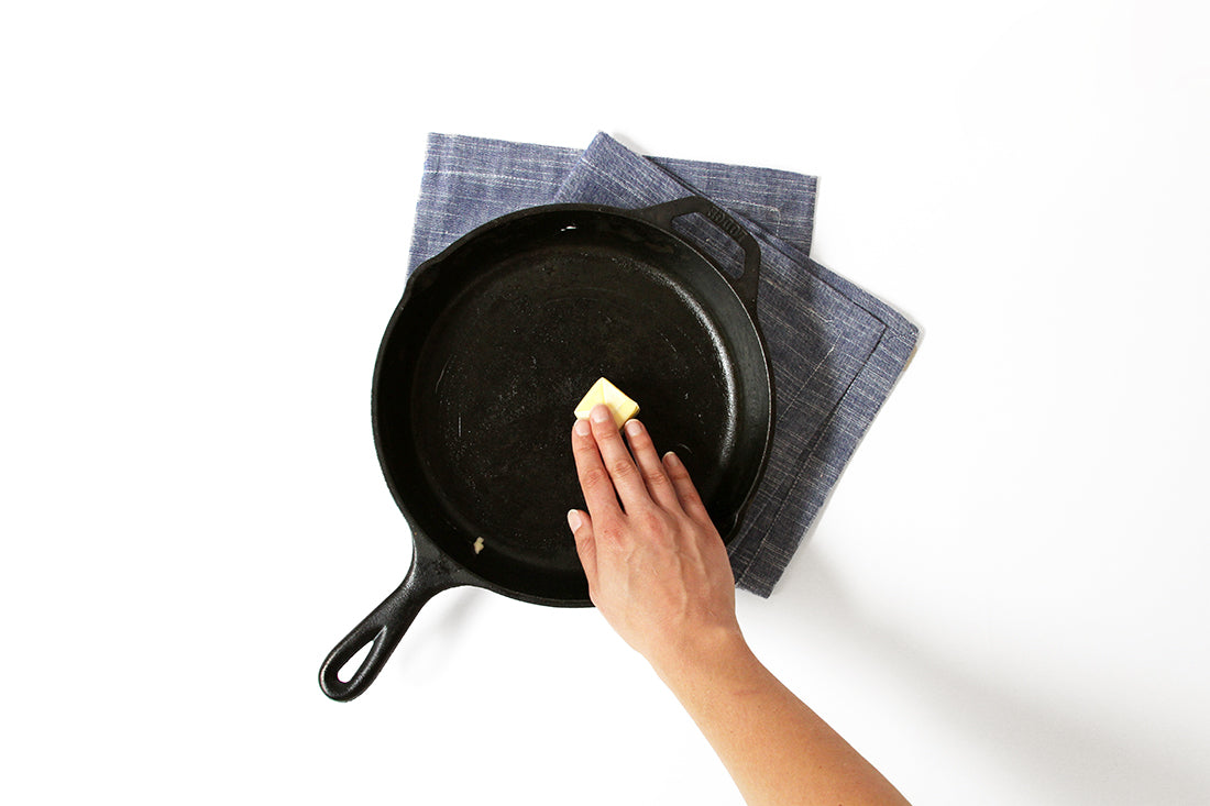 A hand putting a slice of butter onto a skillet used for Miss Jones Baking Co Chocolate Chip Brownie Skillet