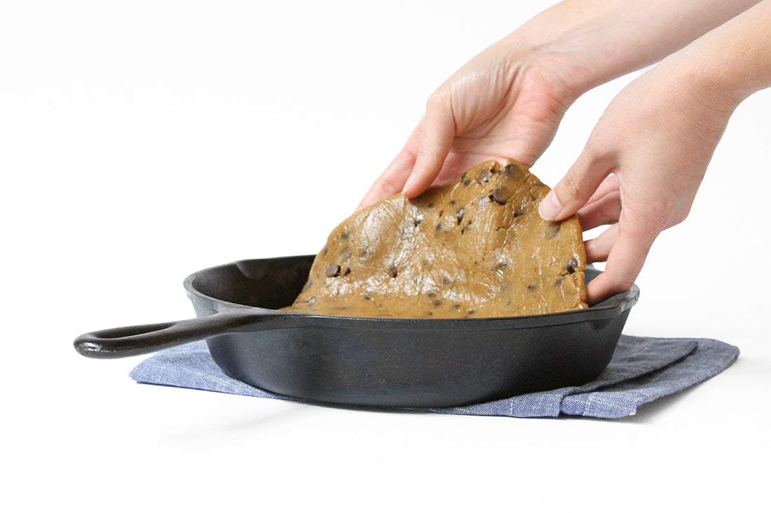 Flattened cookie dough lowered into skillet above brownie batter for Miss Jones Baking Co Chocolate Chip Brownie Skillet