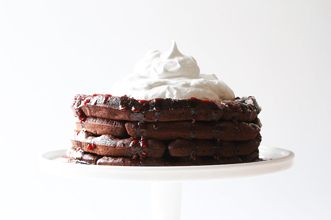 Side image of stack of four Miss Jones Baking Co Chocolate Cake Waffles topped with jam and whipped cream