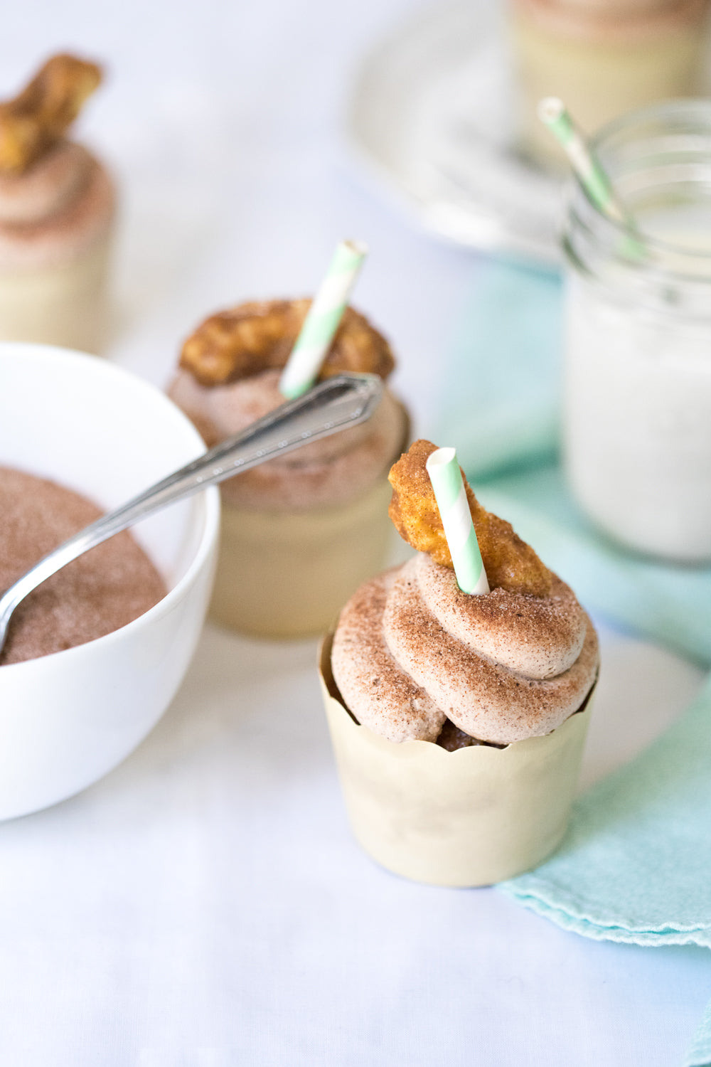 Close up image of a Miss Jones Baking Co Festive Churro Cupcake next to a glass of milk and a bowl of cinnamon sugar