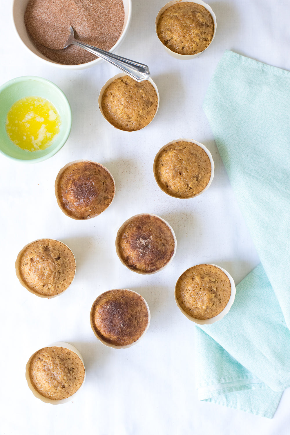 Image of nine Miss Jones Baking Co Festive Churro Cupcakes next to a bowl of cinnamon sugar and a bowl of butter