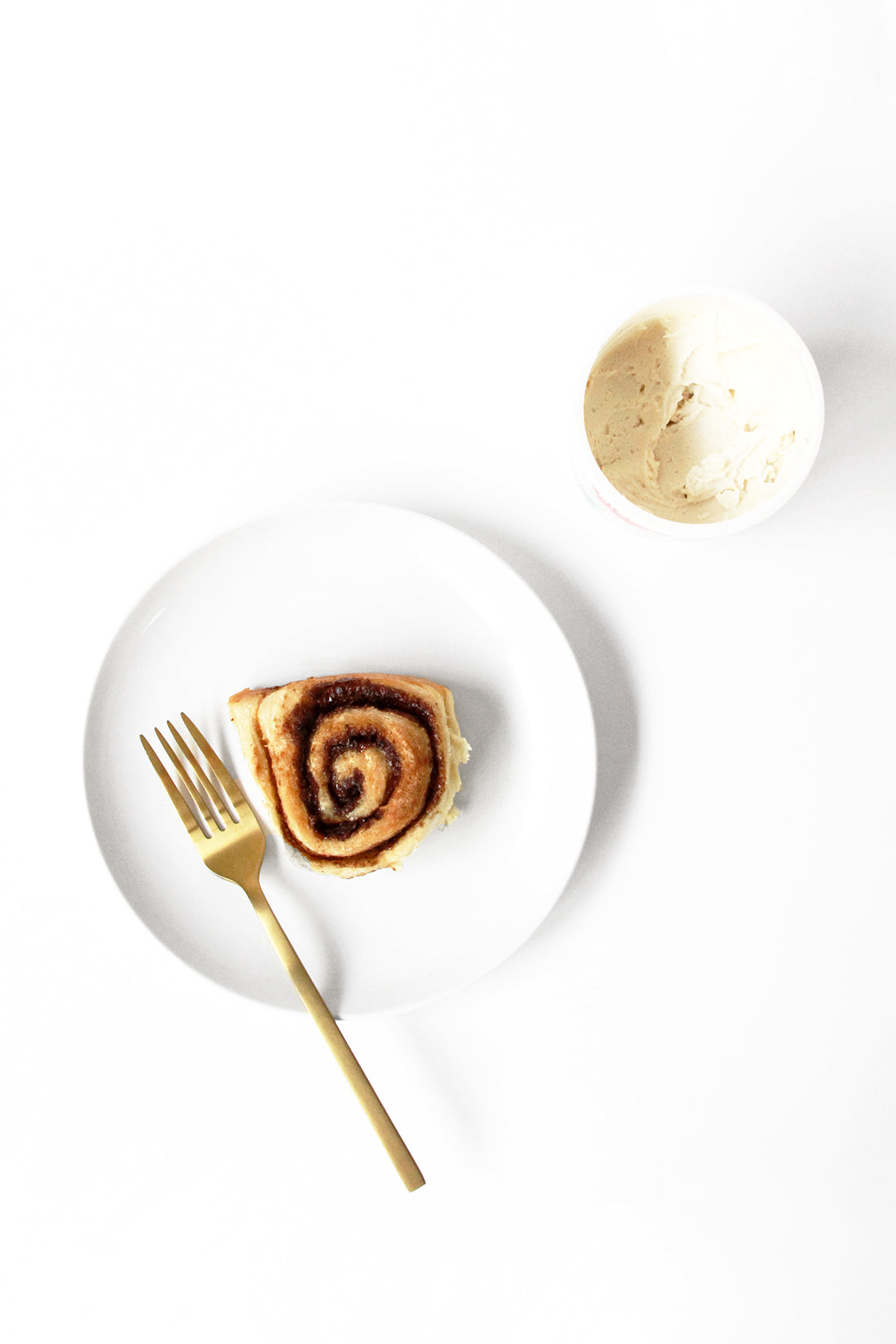 Image from above of a plate with Miss Jones Baking Co Cake Mix Cinnamon Roll next to a container of frosting