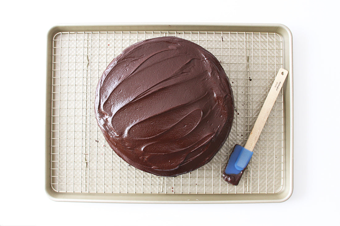 Image of the top of Miss Jones Baking Co Minty Cookie Crunch Cake on a baking rack next to a blue spatula