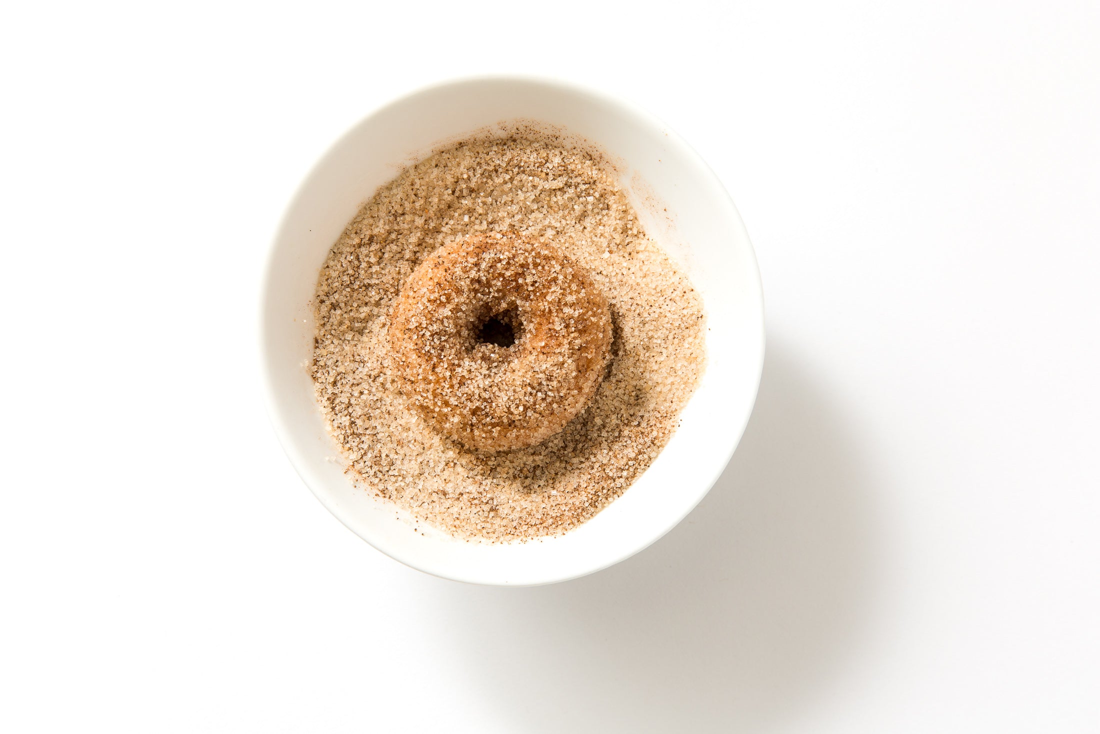 Close up image of a Miss Jones Baking Co Dirty Chai Mini Donut in a bowl of cinnamon sugar