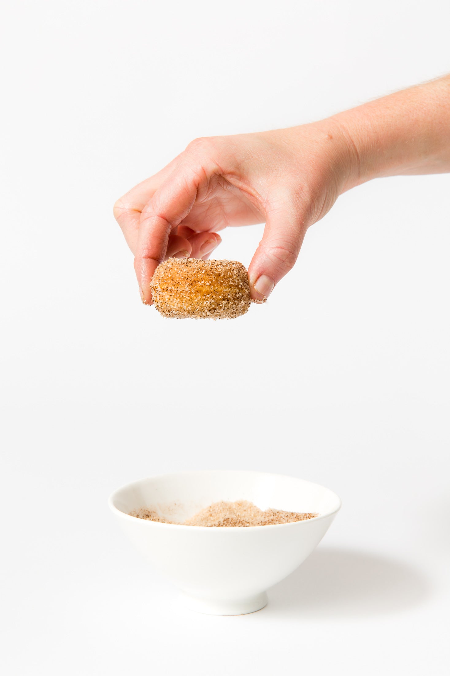 Image of a hand holding a Miss Jones Baking Co Dirty Chai Mini Donut above a bowl of cinnamon sugar