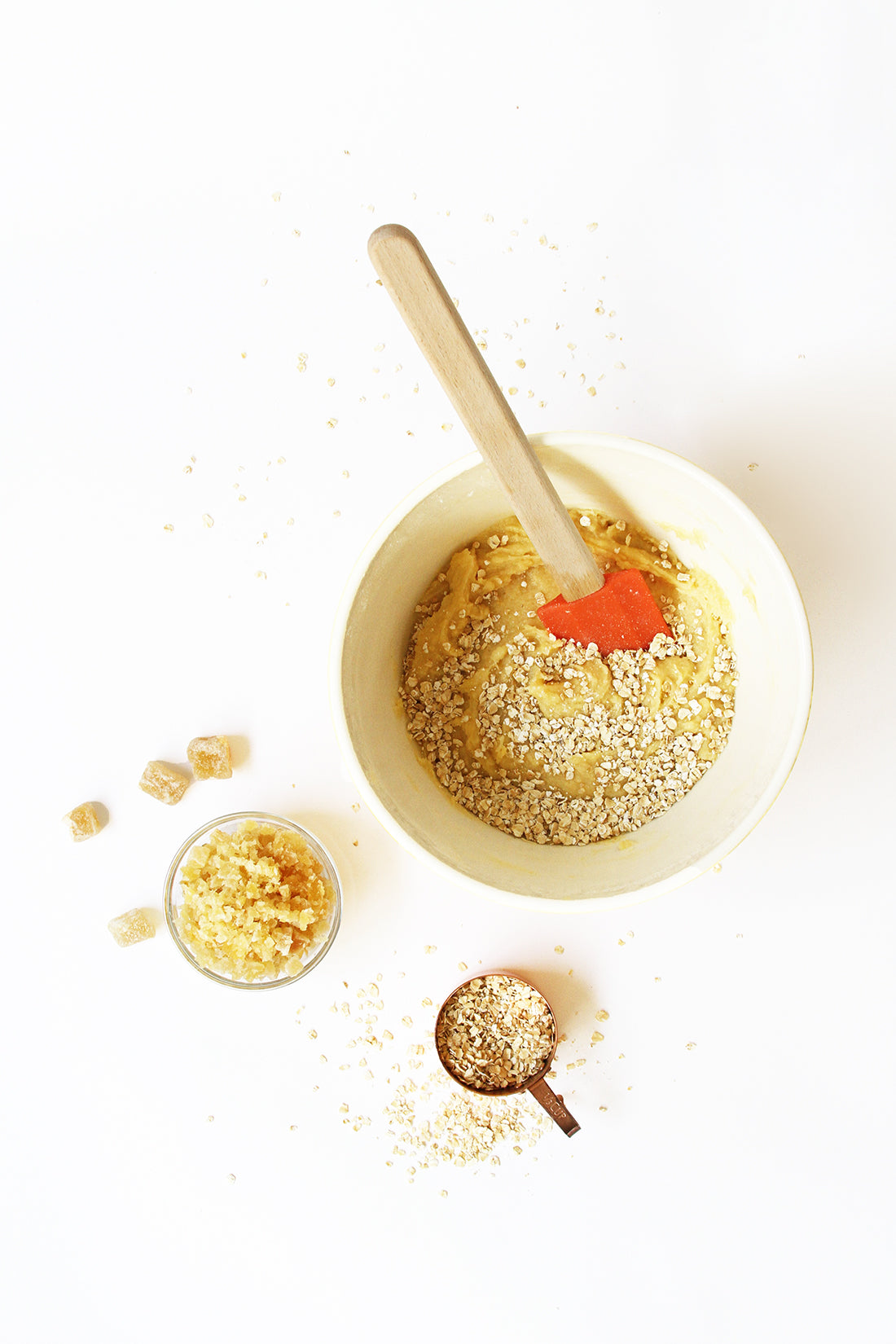 Image of a bowl of Miss Jones Baking Co Ginger Oatmeal Drop Cookies batter next to a measuring cup of oats and a bowl of ginger