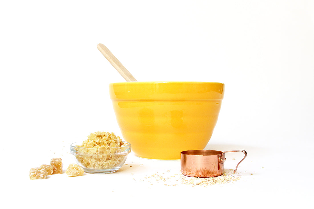 Image of the side of a yellow mixing bowl next to a glass bowl of ginger and a measuring cup of oats for Miss Jones Baking Co Ginger Oatmeal Drop Cookies