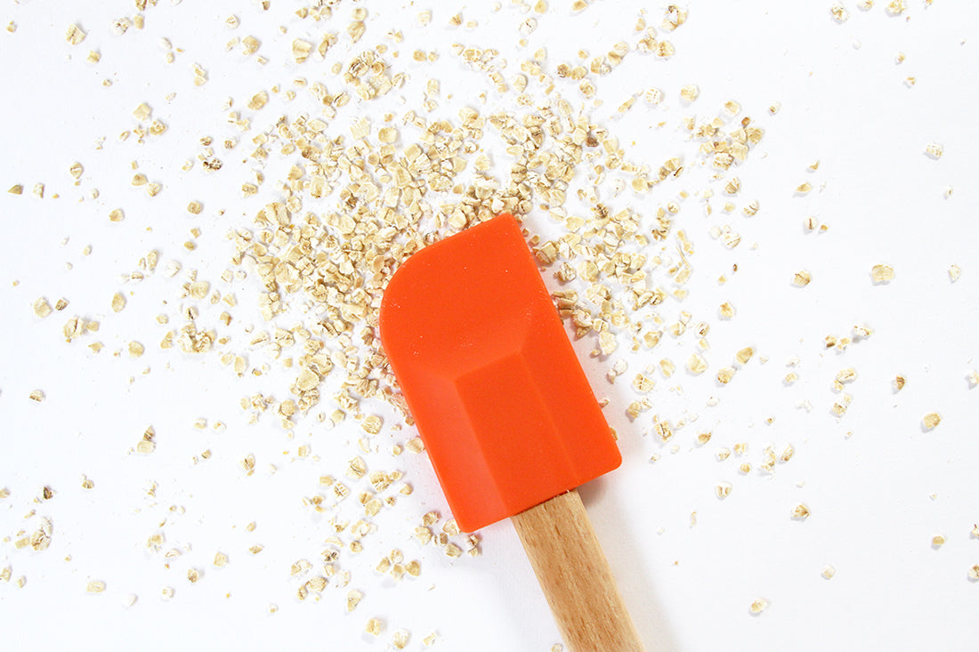 Image of an orange spatula above scattered oats for Miss Jones Baking Co Ginger Oatmeal Drop Cookies recipe