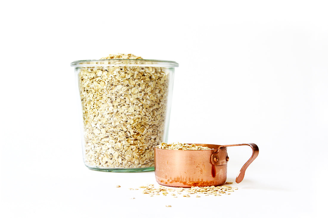 Image of oats in a glass jar next to a coper measuring cup full of oats used for Miss Jones Baking Co Ginger Oatmeal Drop Cookies recipe