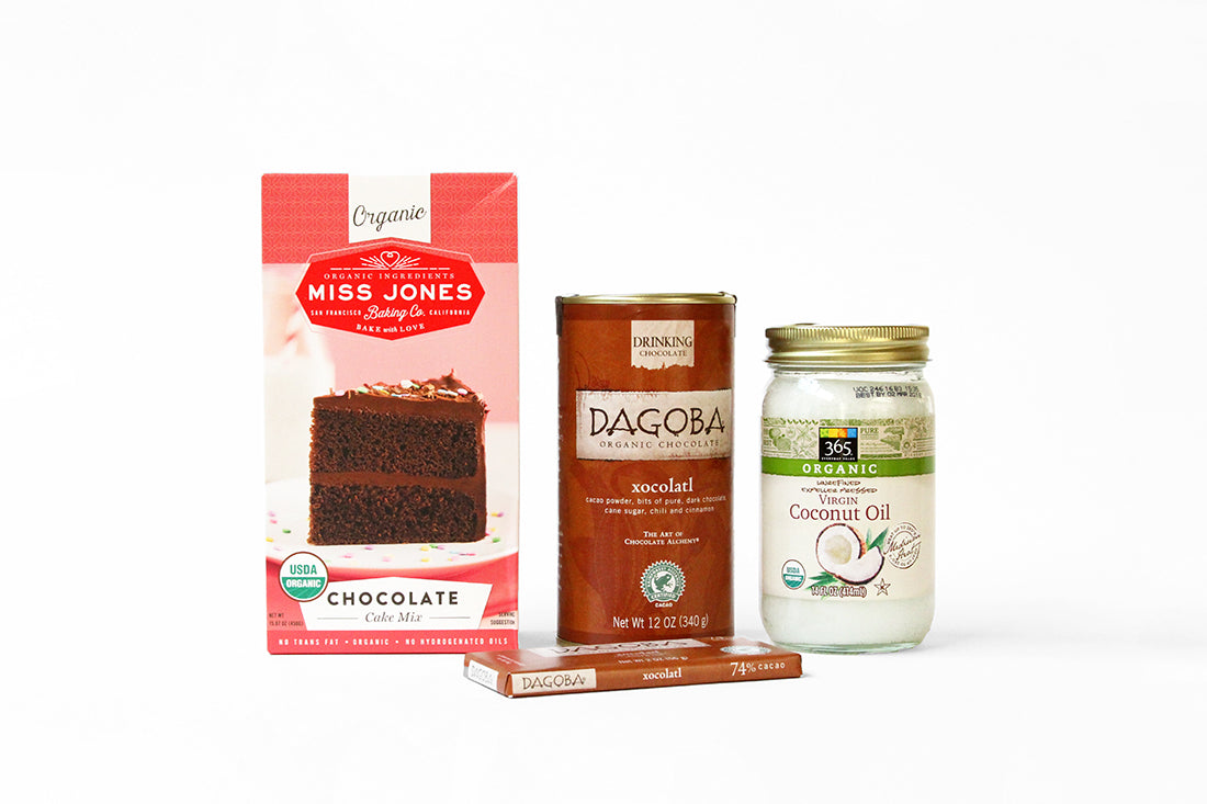 Image of a box of Miss Jones Chocolate Cake Mix next to a jar of Dagoba xocolatl, a bar of chocolate and a jar of coconut oil for Miss Jones Baking Co Hot Cocoa Mug Cake Recipe
