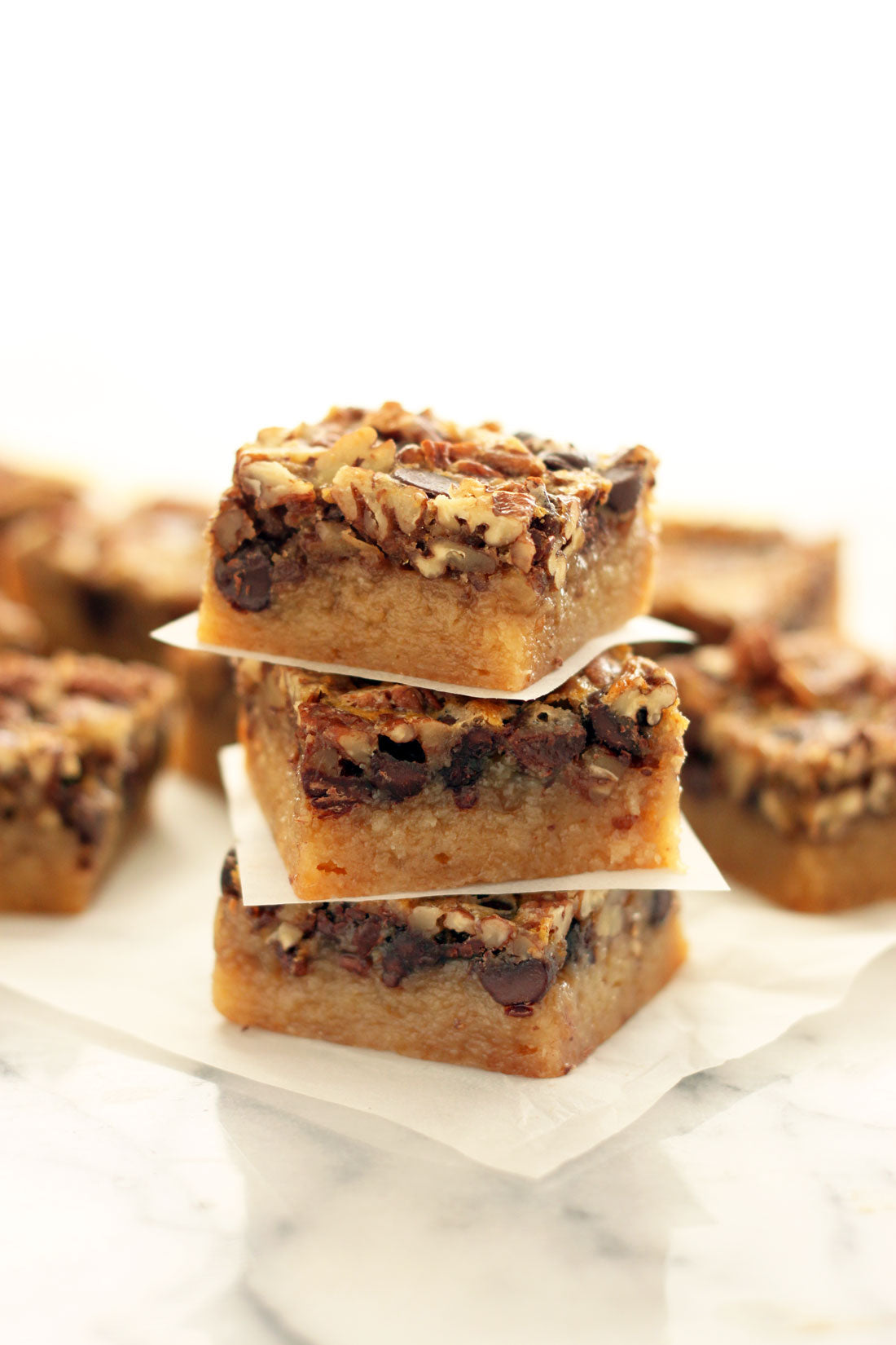 Image of three Miss Jones Baking Co Chocolate Pecan Pie Butter Bars stacked in front of other Miss Jones Baking Co Chocolate Pecan Pie Butter Bars