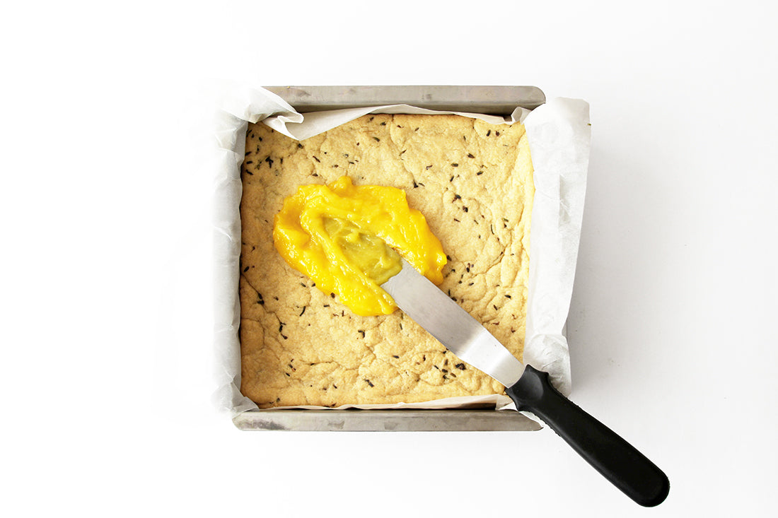 Image from above of a knife spreading lemon filling onto lavender crust for Miss Jones Baking Co Lavender Lemon Bars 