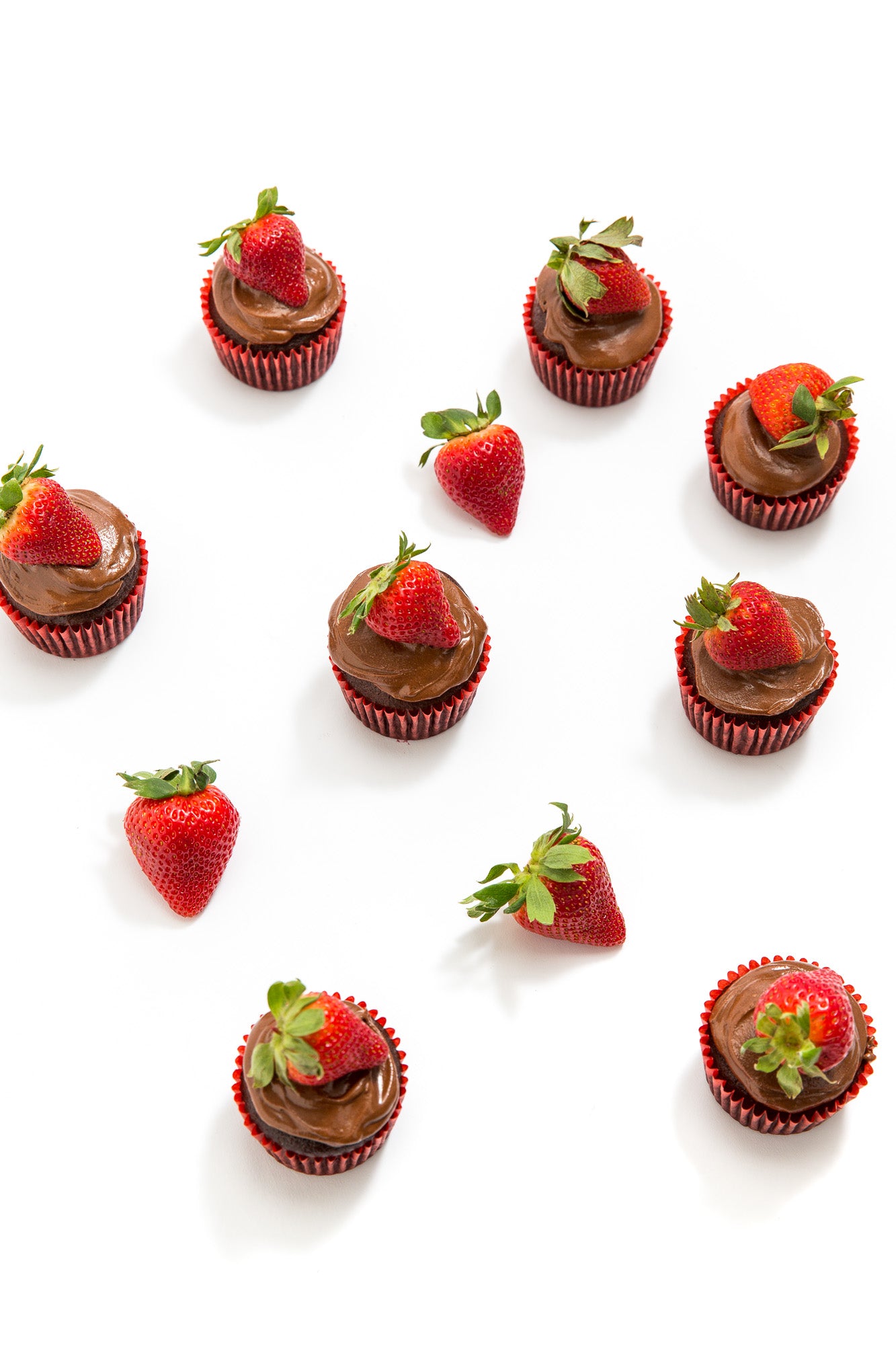 Image from above of eight Miss Jones Baking Co Chocolate Hazelnut Strawberry Cupcakes scattered around a couple of strawberries