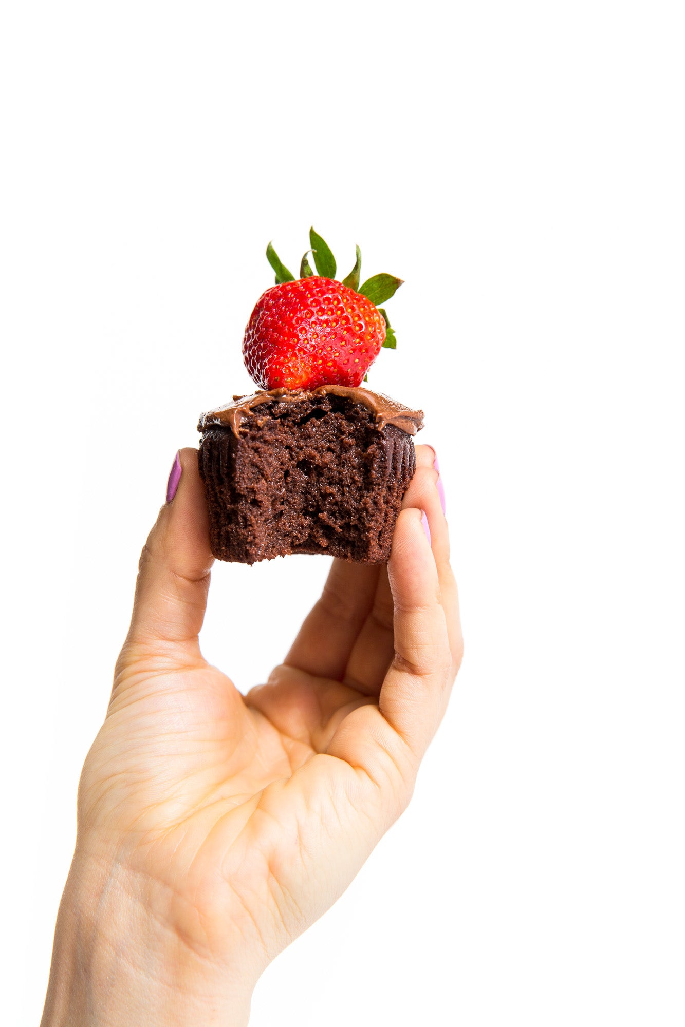 A hand holding a half eaten Miss Jones Baking Co Chocolate Hazelnut cupcake with a strawberry on top