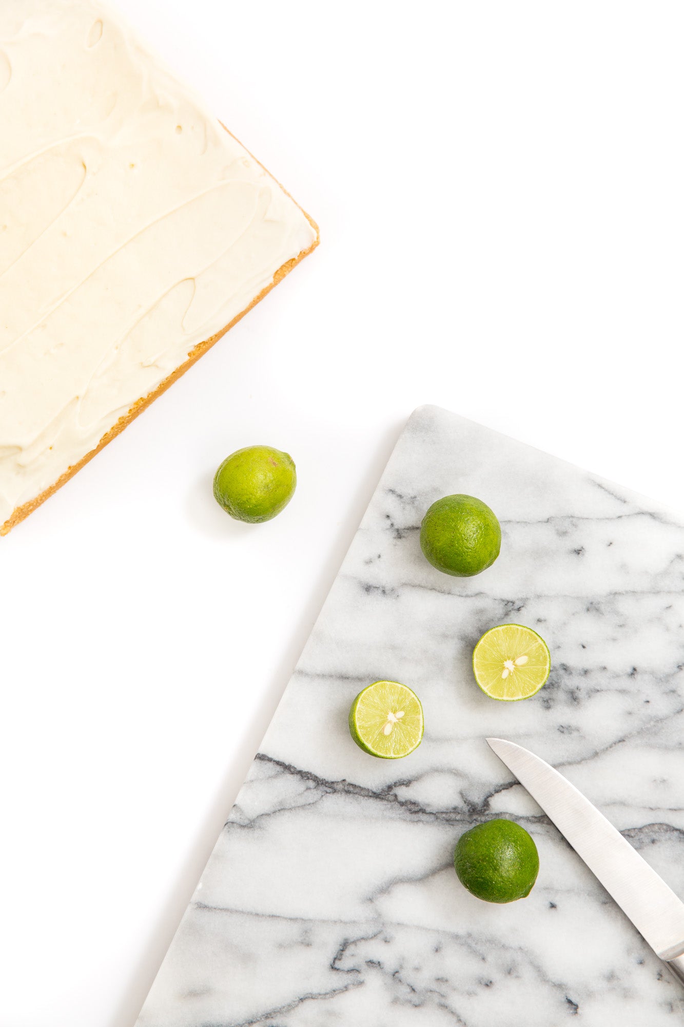 Image of part of Miss Jones Baking Co Key Lime Margarita Bars next to a marble cutting board with limes and a knife