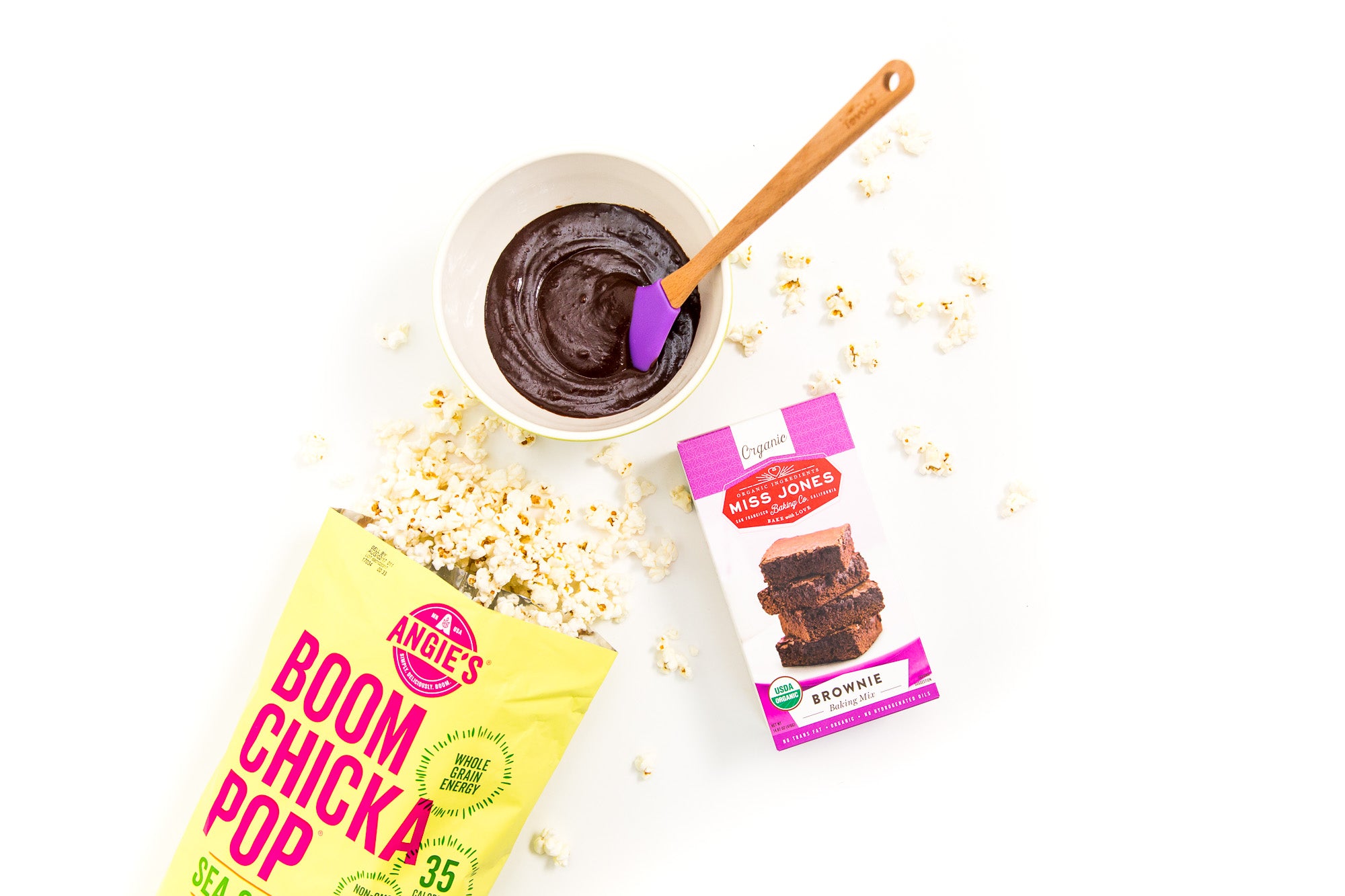 Image from above of a box of Miss Jones Brownie Mix next to a bag of Boom Chicka Pop Sea Salt Popcorn and a bowl of chocolate for Miss Jones Baking Co Popcorn Brownies Recipe