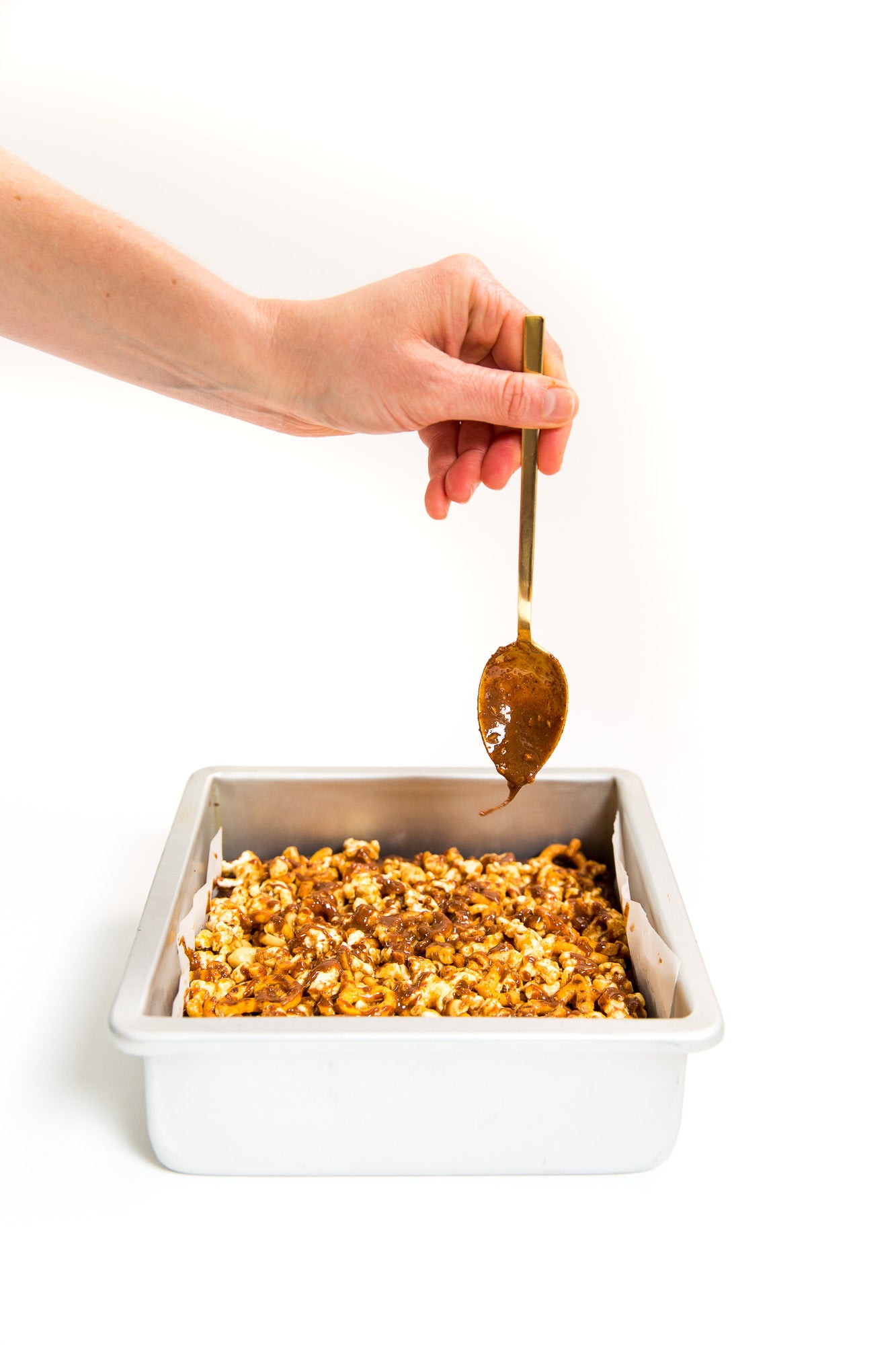 Image of a hand drizzling caramel from a spoon onto Miss Jones Baking Co Popcorn Brownies