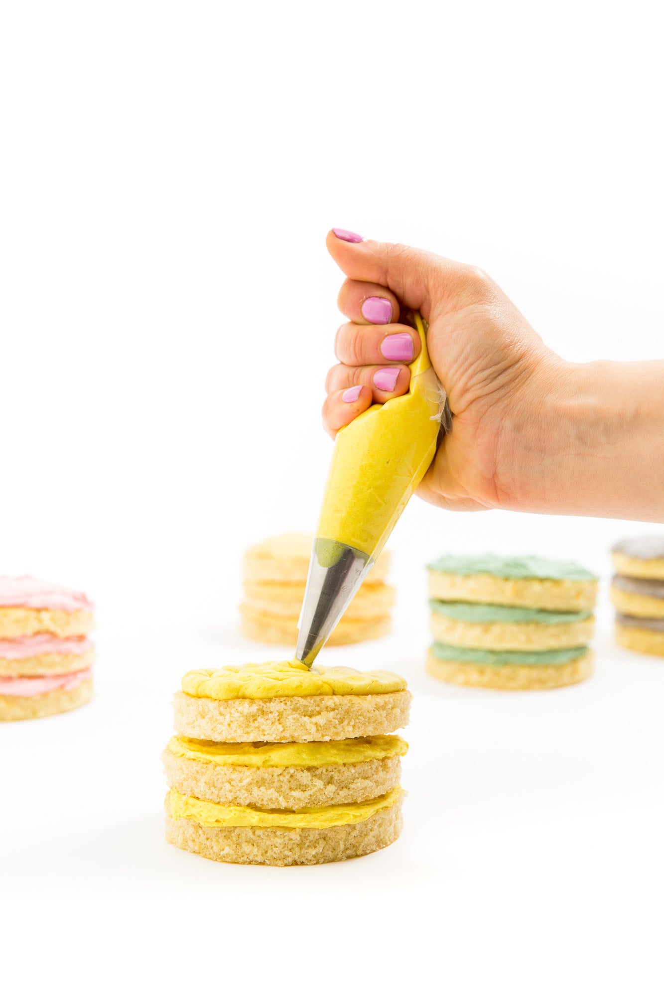 Image from the side of a hand frosting a yellow Miss Jones Baking Co Rainbow Cakelet