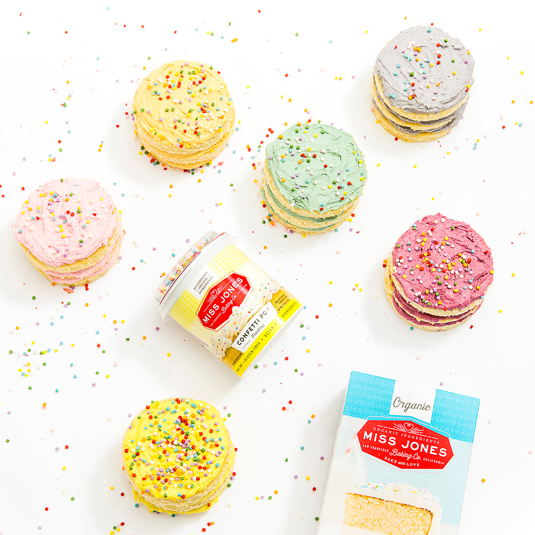 Image from above of Miss Jones Baking Co Rainbow Cakelets next to a jar of Miss Jones Cream Cheese Frosting and a box of Miss Jones Vanilla Cake Mix
