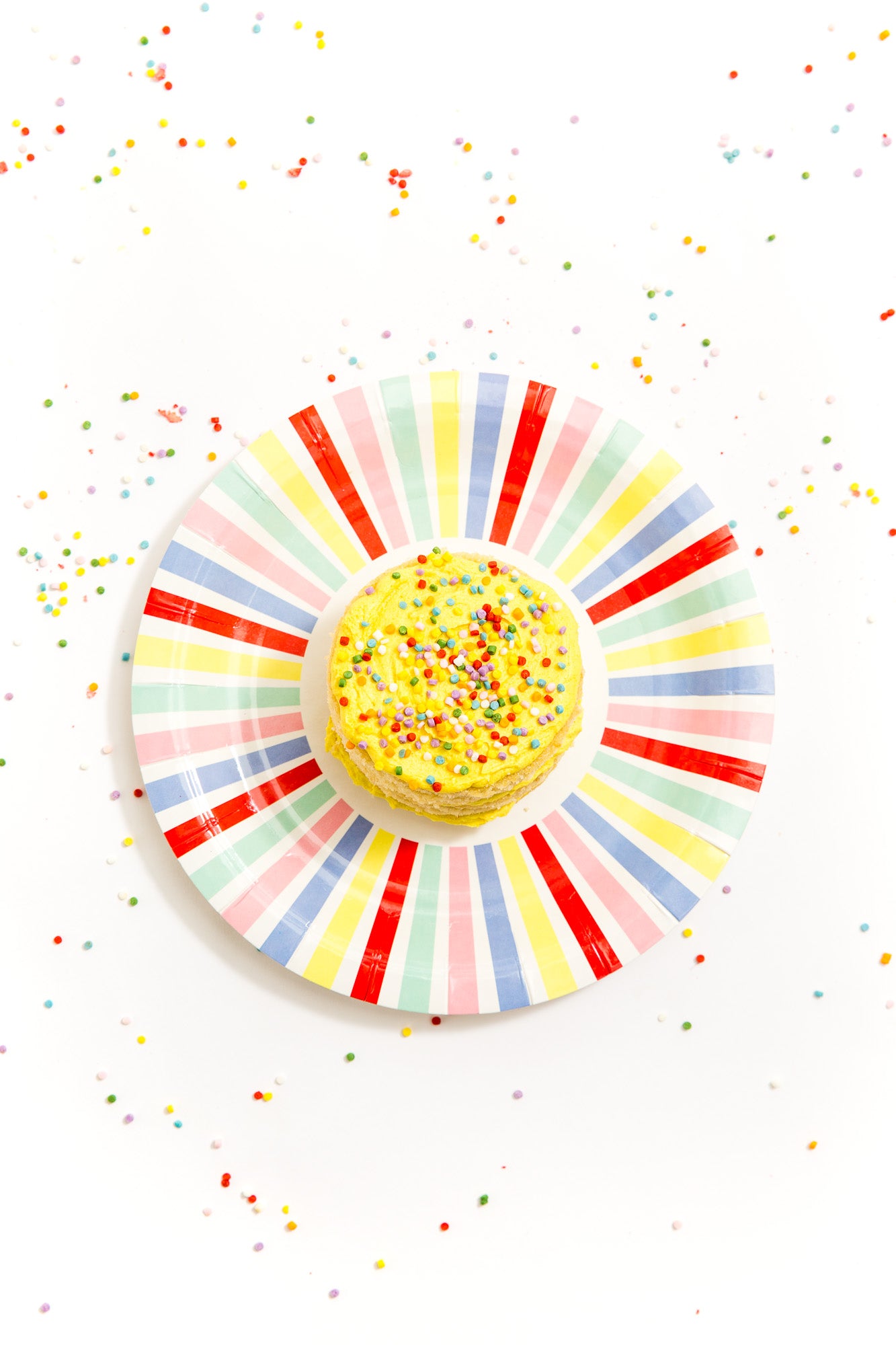 Image from above of a Miss Jones Baking Co Rainbow Cakelet on a rainbow plate surrounded by sprinkles