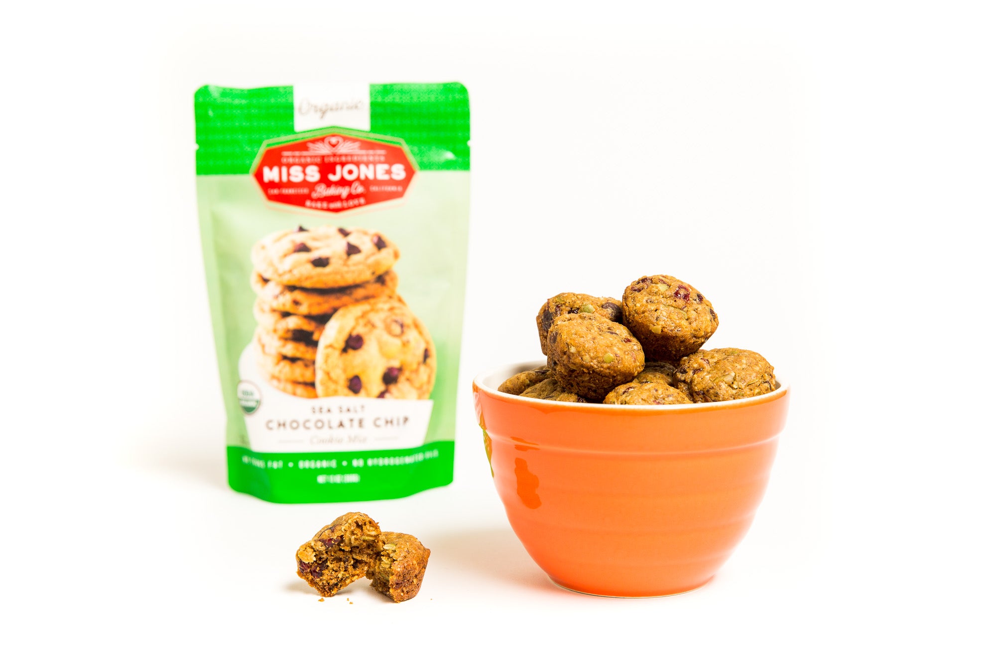 Image of a bag of Miss Jones Chocolate Chip Cookie Mix behind an orange bowl of Miss Jones Baking Co Happy Trails Mix Cookie Bites 