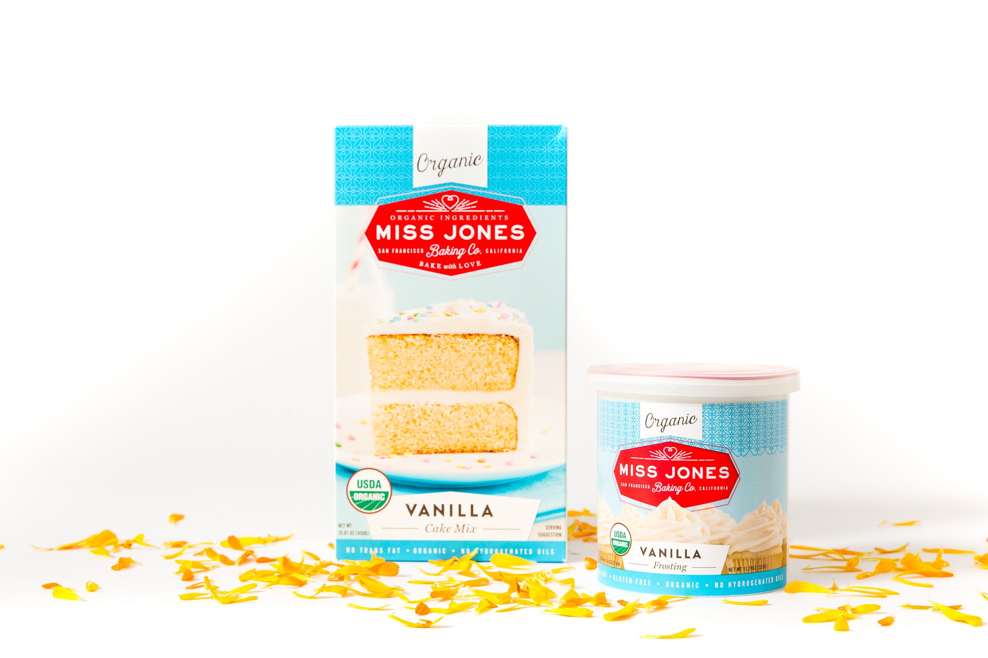 Image of a box of Miss Jones Vanilla Cake Mix and a jar of Miss Jones Vanilla Frosting surrounded by yellow flower petals for Miss Jones Baking Co Floral Bloom Layer Cake