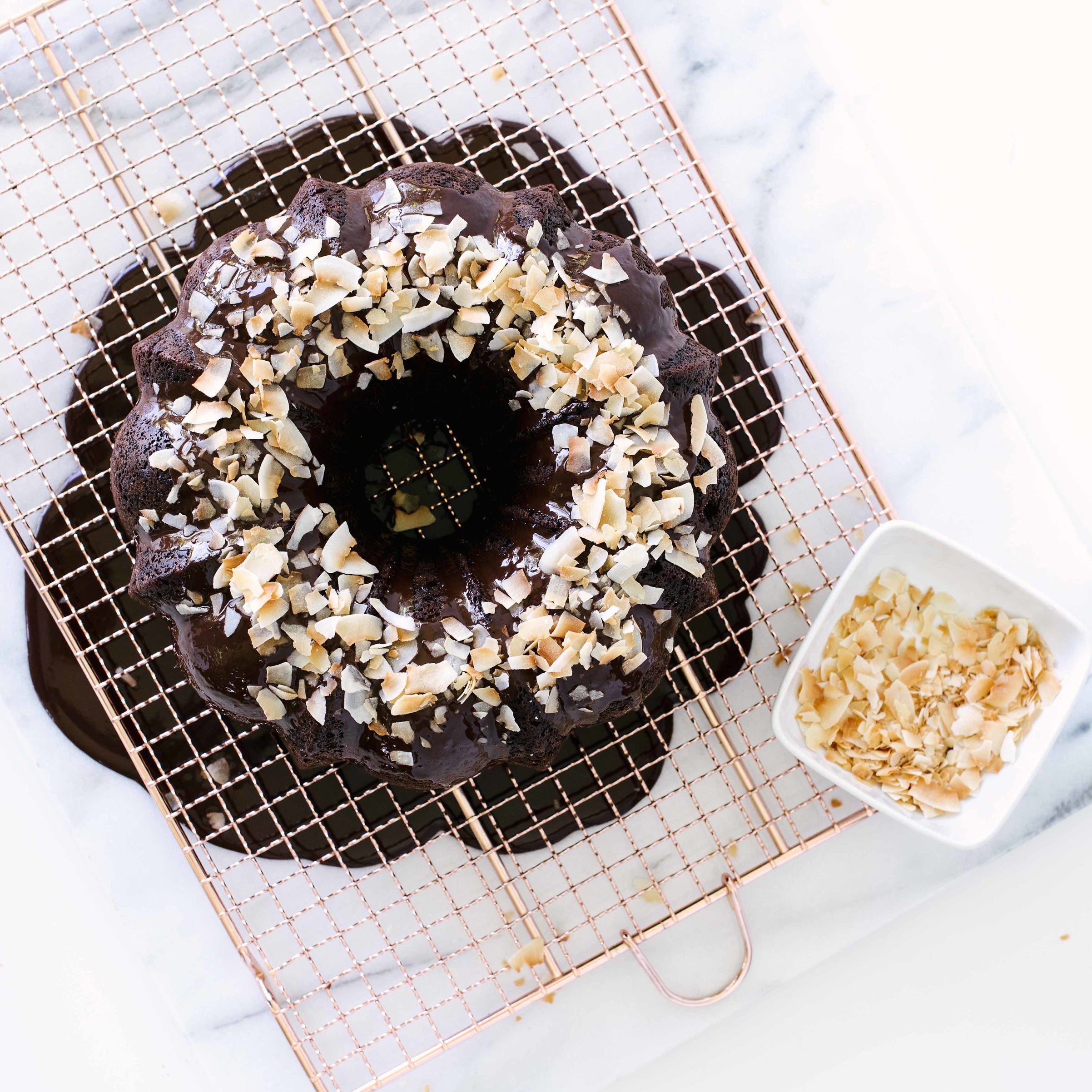 Top of Miss Jones Dark Chocolate Coconut Bundt Cake on a baking sheet with toasted coconut flakes on the cake and in a bowl to the side